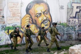 Israeli soldiers patrol in front of a mural of jailed Fatah leader Marwan Barghouti that was painted on Israel&#039;s separation wall in the occupied West Bank [File: Nasser Shiyoukhi/AP]