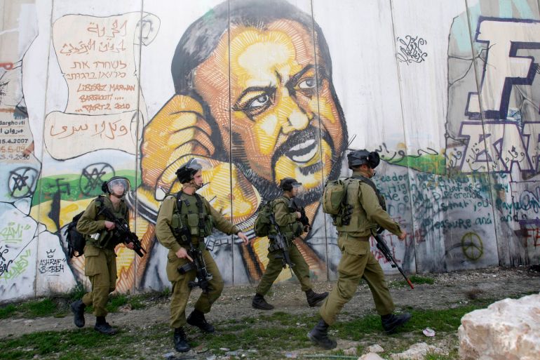 In the background of part of Israel's separation barrier with portrait of jailed Fatah leader Marwan Barghouti, Israeli soldiers patrol at Kalandia checkpoint between Jerusalem and the West Bank city of Ramallah,