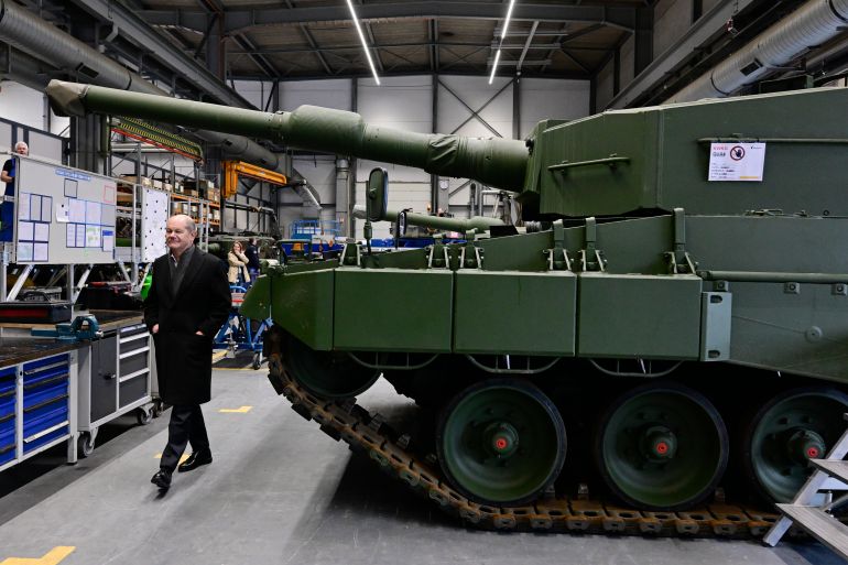 a man wearing black walks past a tank in a factory