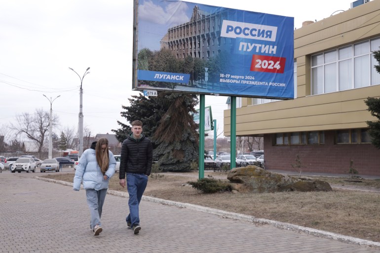 A couple walk past a billboard which promotes the upcoming presidential election with words in "Russian: Russia, Putin, 2024" in a street in Luhansk, the capital of Russian-controlled Luhansk region, eastern Ukraine, on Thursday, March 14, 2024. Russian President Vladimir Putin Thursday called on people in Ukraine's occupied regions to vote, telling them and Russians that participation in the elections is "manifestation of patriotic feeling," Presidential elections are scheduled in Russia for March 17. (AP Photo)
