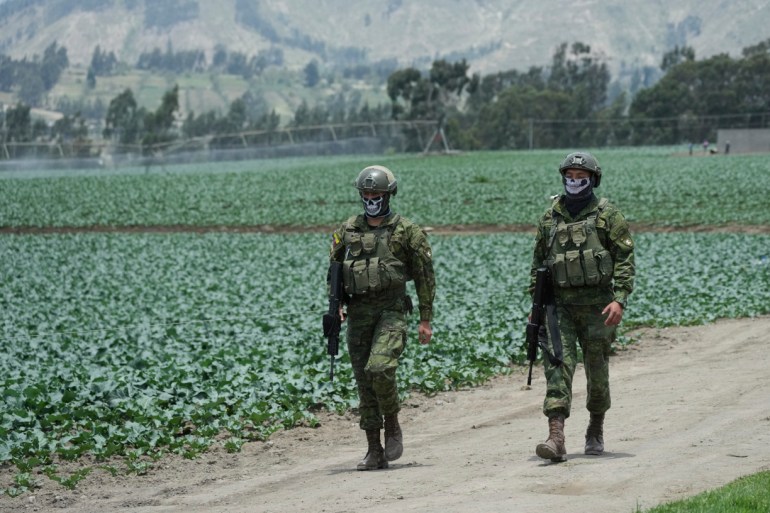 Soldiers in fatigues and combat gear walk through fields in rural Ecuador.