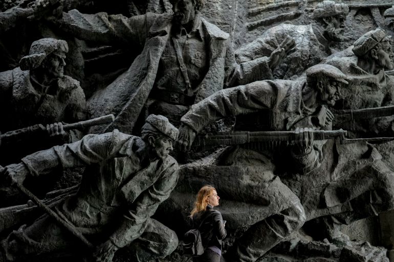 A woman walking in front of bas-relief sculptures depicting war scenes in the National Museum of the History of Ukraine in the Second World War in Kyiv. She looks tiny in comparison with the sculptures.