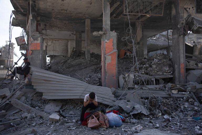 a man sits with his head in his hands in front of a destroyed building