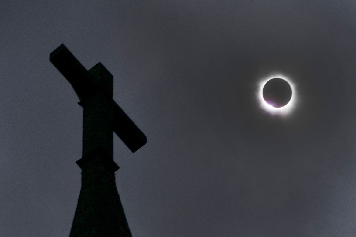 A cross is seen against a darkened sky, as a solar eclipse occurs in the background.