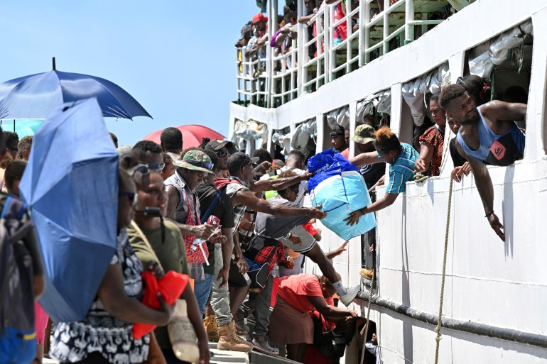 Crowds of people on the pier and others on board a ferry as they head back home for the elections. Some are shielding themselves from the sun beneath umbrellas. Others are passing luggage to those on board.