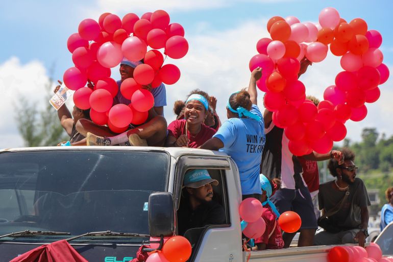 People in Solomon Islands holding red balloons at a campaign rally. They're crowded on the back of a small lorry.