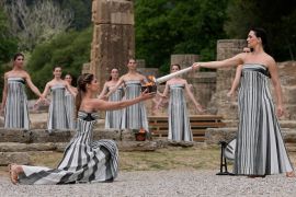 Actress Mary Mina, playing high priestess, right, lights a torch during the official ceremony of the flame lighting for the Paris Olympics, at the Ancient Olympia site, Greece, on April 16, 2024 [Thanassis Stavrakis/AP Photo]