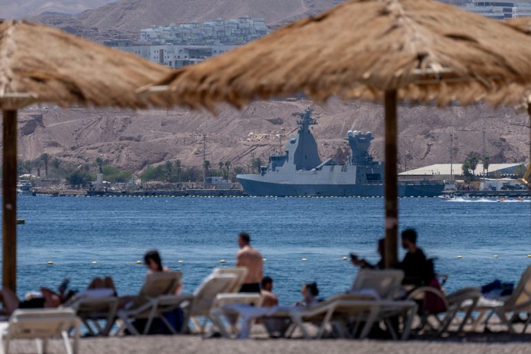 people sit on a beach with a war ship in the background