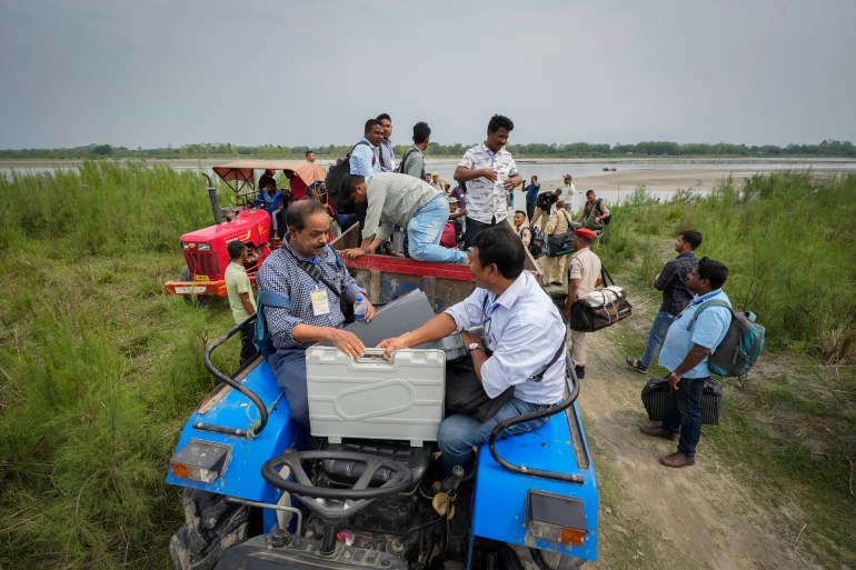 Polling officials carrying electronic voting machines and security personnel board on a tractor after disembarking from a boat