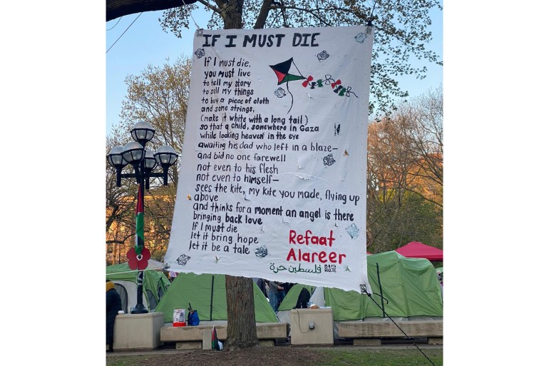 A poster with the text of a poem by Palestinian poet Refaat Alareer hung on a tree, in the background tents