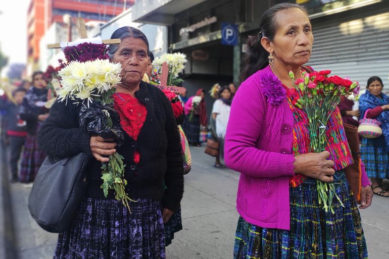 Indigenous women in Guatemala hold bouquets of flowers as they walk through the streets.