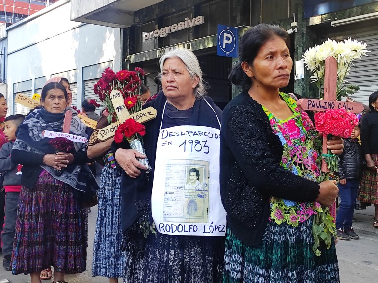 Indigenous women in Guatemala march, some with bouquets of flowers, some with crosses, others with black-and-white photos of their loved ones around their necks.