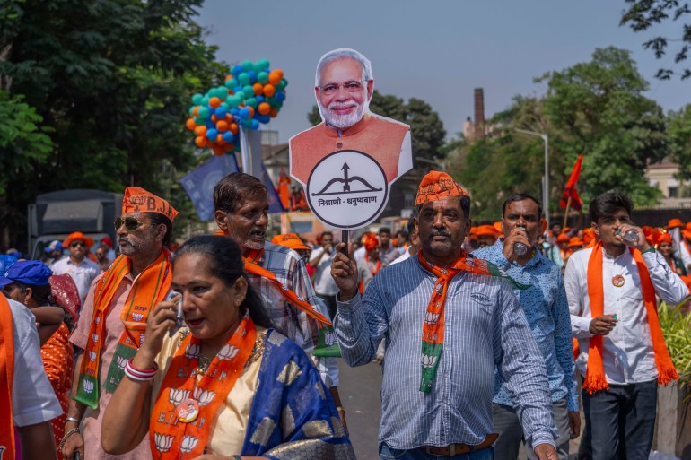 Supporters of National Democratic Alliance walk in a road show as one of them holds a cutout photo of Indian Prime Minister Narendra Modi as their candidates arrive to file nomination papers ahead of national elections in Mumbai, India, Monday, April 29, 2024. (AP Photo/Rafiq Maqbool)