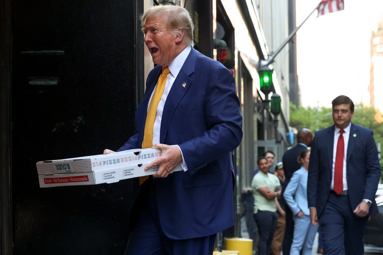 Donald Trump walks with two boxes of pizza in his hands, his mouth slightly agape.