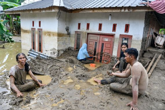 Residents clear deep mud from the entrance of an inundated home.