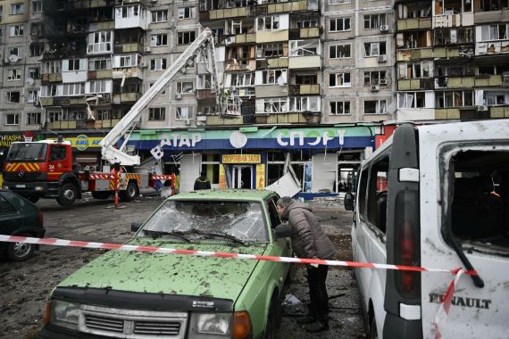 A local resident inspects a damaged car in front of a damaged residential building following an air attack in Kyiv