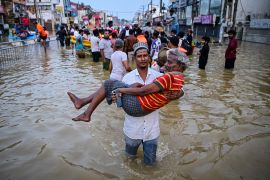 A youth carries an elderly man as they wade through a flooded street after heavy rainfall in Wellampitiya on the outskirts of Colombo on Sunday [Ishara S Kodikara/AFP]