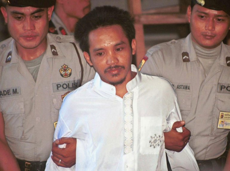 Ali Imronm dressed in a white short and escorted by two police officers, was found guilty in the Bali Bombings in an Indonesian court