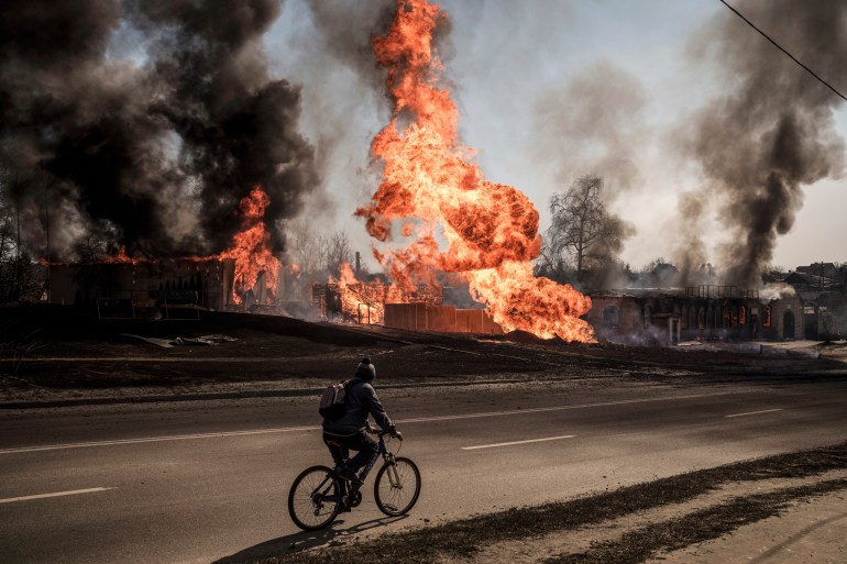 A man rides his bicycle past flames and smoke rising from a fire following a Russian attack in Kharkiv