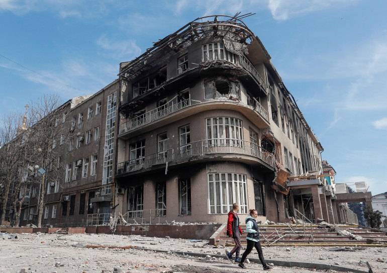 Residents walk near a building destroyed in the course of the Ukraine-Russia conflict, in the southern port city of Mariupol