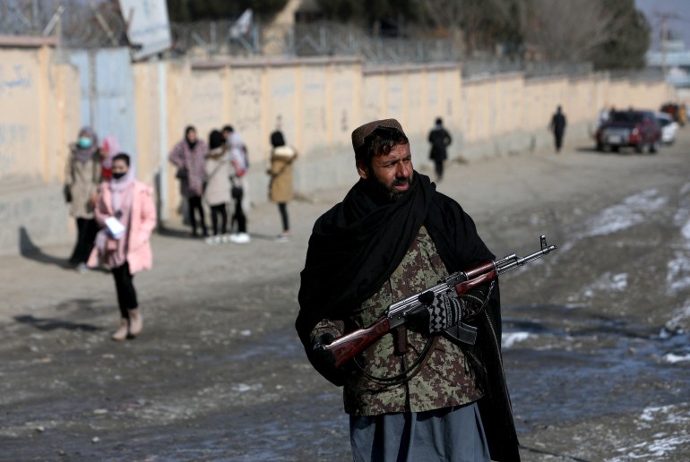 A photo of a Taliban fighter standing in a street and holding a gun.