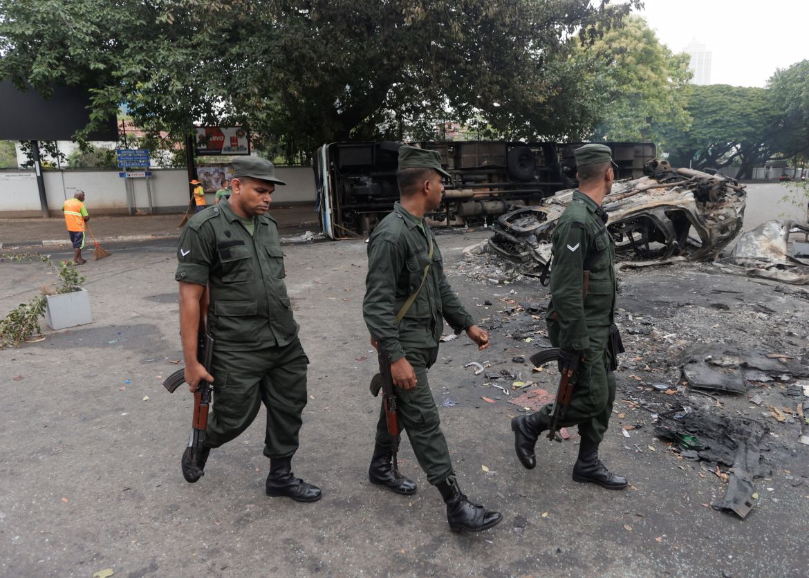 Army soldiers walk past damaged vehicles of Sri Lanka's ruling party supporters after they were set on fire during a clash of pro and anti-government demonstrators near the Prime Minister's official residence