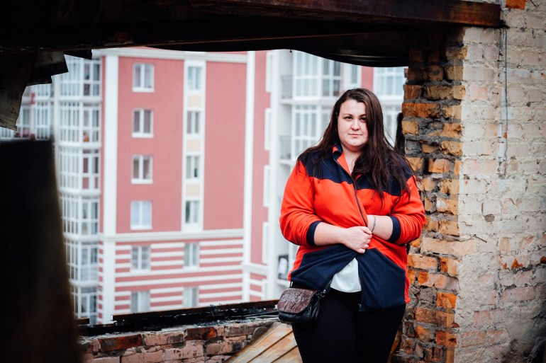 A photo of Anna Hlyvenko standing in front of a large hole on the side of an apartment building that once had a window.