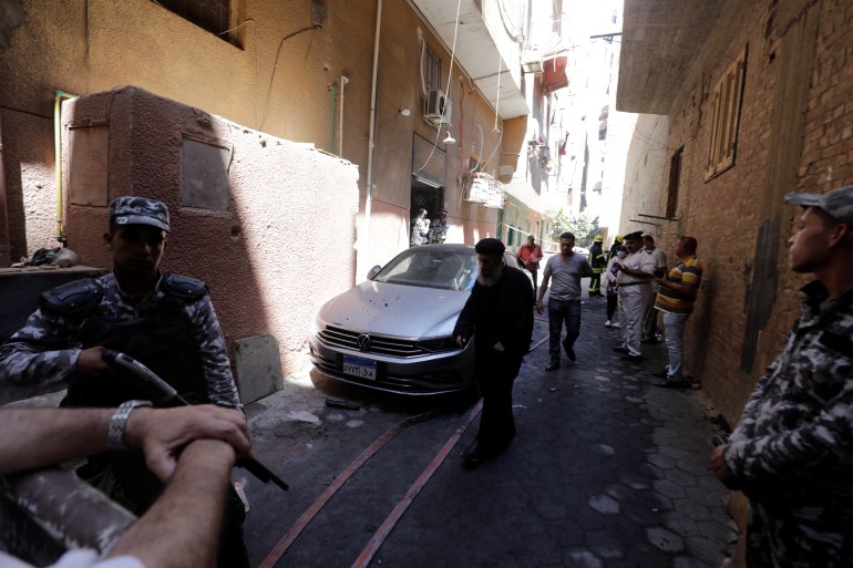 People and policemen stand near the scene where a deadly fire broke out at the Abu Sifin church in Giza