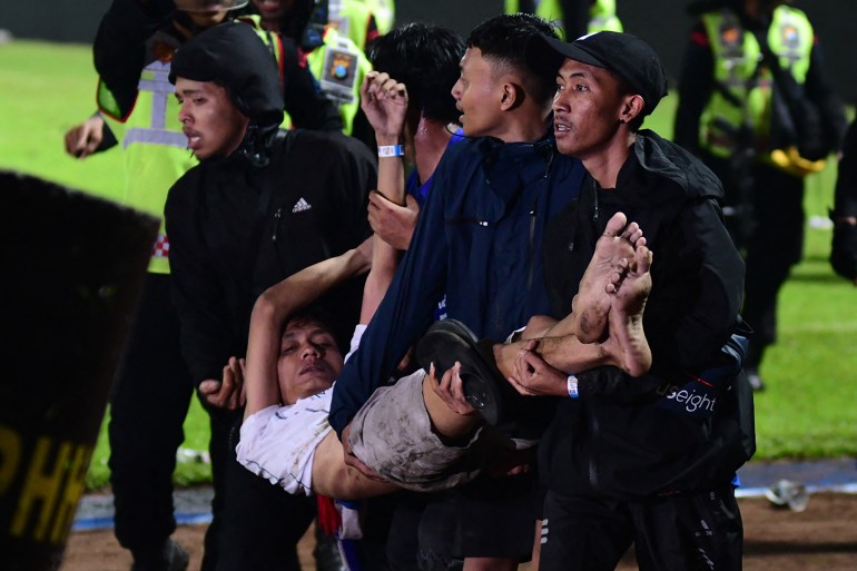 In this picture taken on October 1, 2022, a group of people carry a man after a football match between Arema FC and Persebaya Surabaya at Kanjuruhan stadium in Malang
