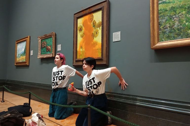 A handout picture from the Just Stop Oil climate campaign group shows activists with their hands glued to the wall under Vincent van Gogh's "Sunflowers" after throwing tomato soup on the painting at the National Gallery in central London on October 14, 2022. - London's Metropolitan Police said its officers arrested two protesters from the Just Stop Oil group for criminal damage and aggravated trespass after they "threw a substance over a painting" at the gallery on Trafalgar Square. (Photo by Handout / Just Stop Oil / AFP) / RESTRICTED TO EDITORIAL USE - MANDATORY CREDIT "AFP PHOTO / JUST STOP OIL " - NO MARKETING - NO ADVERTISING CAMPAIGNS - DISTRIBUTED AS A SERVICE TO CLIENTS
