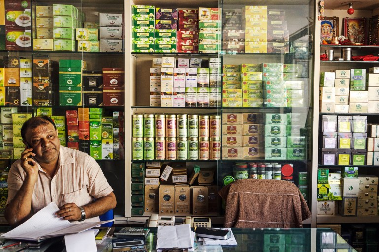 Shopkeeper speaks on his mobile phone with a display of tea behind him