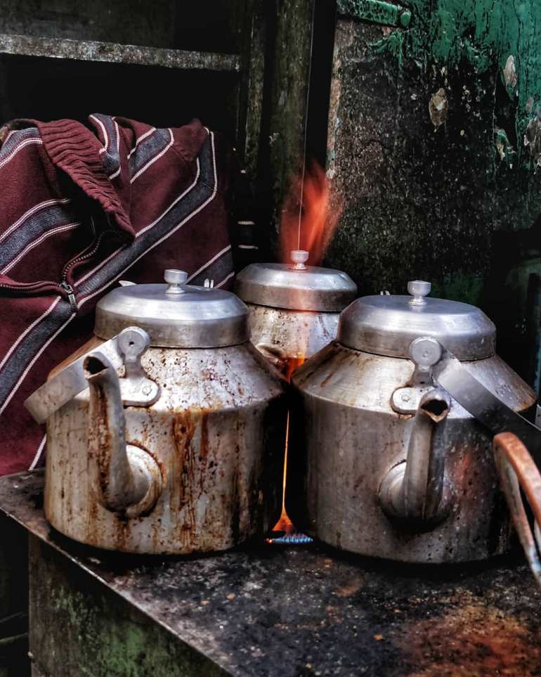 Three teapots boiling on a primitive stove in a street tea stall