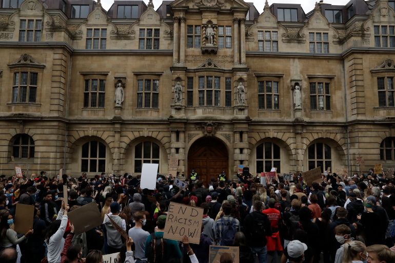 Supporters of the Rhodes Must Fall group, participate in a protest calling for the removal of a statue of Cecil Rhodes, a Victorian imperialist in southern Africa who made a fortune from mines and endowed the university's Rhodes scholarships, beneath the statue which stands on the facade, seen top centre, of Oriel College, in Oxford, England, Tuesday, June 9, 2020. More statues of imperialist figures could be removed from Britain's streets, following the toppling of a monument to slave trader Edward Colston in the city of Bristol, the mayor of London said Tuesday. (AP Photo/Matt Dunham)