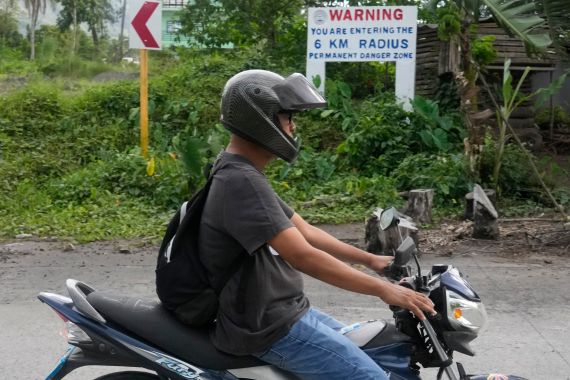 A man passes by a warning sign along a road in Mabinit, located near Mayon volcano